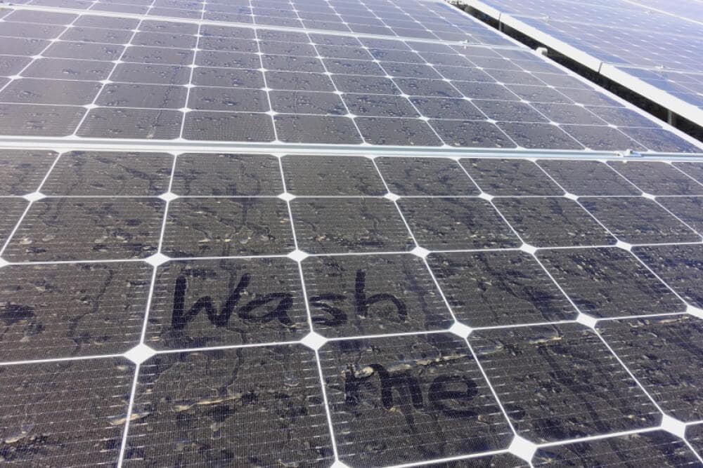 Dirty and dusty solar panels with the words wash me