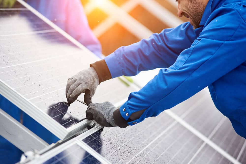 Worker in blue uniform installing solar panels on the roof