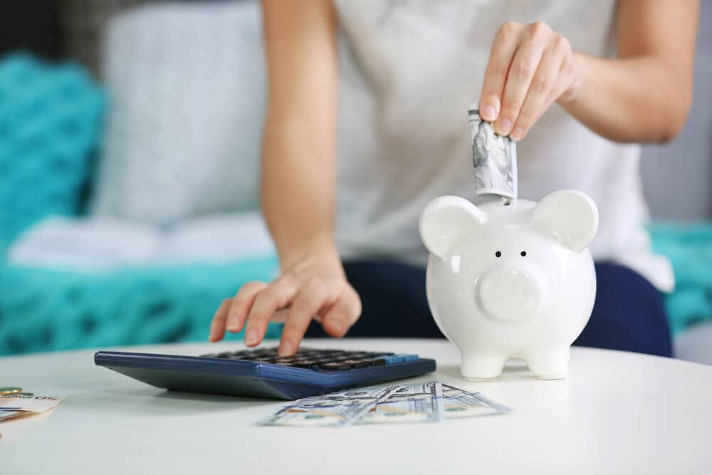 woman using calculator and putting money in piggy bank