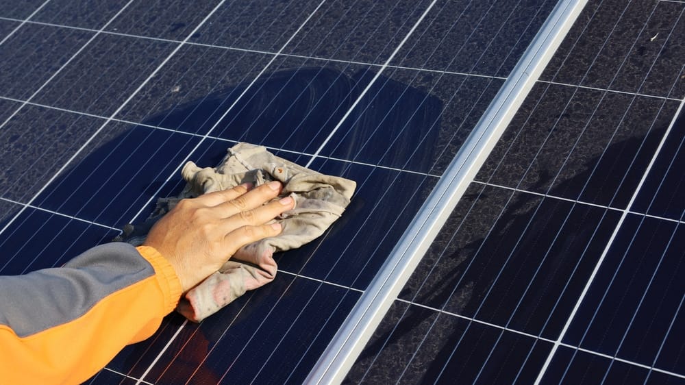 closeup of hand cleaning dusty solar panels with cloth