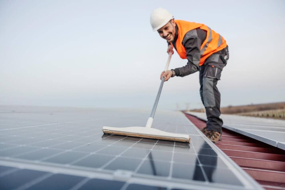 happy worker cleaning solar panels on roof