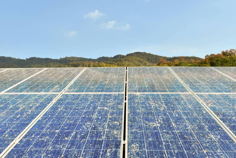 rows of dirty solar panels with background of mountains